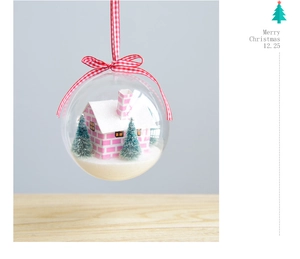 Detail of clear Christmas ball with pink miniature house, snowy trees and plaid ribbon bow