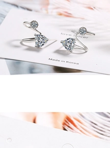 Macro shot of silver heart-shaped zircon earrings on a white card with soft feathers