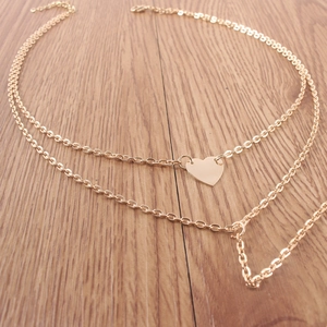 Détail du collier double rang doré avec pendentif cœur sur fond de bois naturel