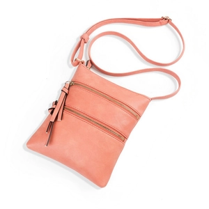 Detail of coral pink crossbody bag with triple zipper pockets and tassel charm