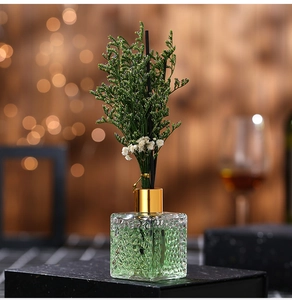 Close-up of green reed diffuser in square glass bottle with gold cap and dried flowers