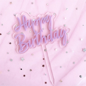 Macro view of purple acrylic Happy Birthday cake topper on pink sparkling mesh background