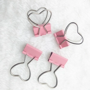 Close-up of four pink heart-shaped metal binder clips on a soft white fluffy background