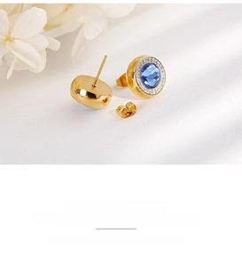 Detail of gold crystal earrings with blue gemstone centers and white zircon accents