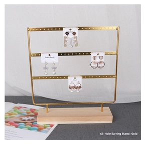 Macro detail of a golden 69-hole metal earring display stand with solid wood base
