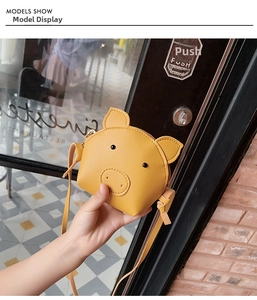 Detail of a mini yellow cartoon pig crossbody bag held in hand to show its small size