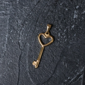 Detailed macro view of a vintage gold heart key pendant on a dark slate stone surface