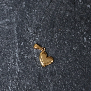 Macro view of polished heart-shaped gold pendant on dark textured stone surface