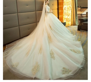 Detail of off-white bridal gown featuring gold lace embroidery and long cathedral train