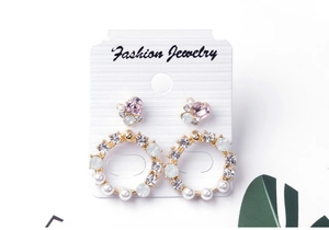 Detail view of gold earrings with pink hearts, pearls, and rhinestones on white card