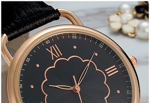 Macro shot of rose gold watch case with black petal texture dial and leather strap