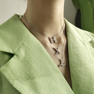 Close-up of S925 sterling silver letter pendants with sparkling pavé diamonds on a model