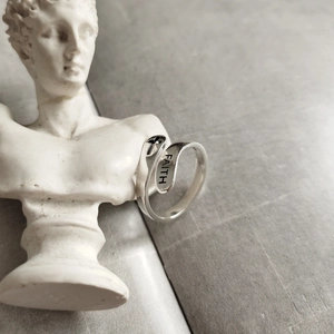 Artistic detail of 925 silver FAITH cross open ring on white classical sculpture