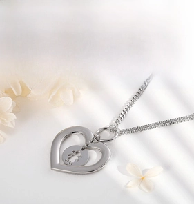 Detail of silver heart pendant necklace with cutout girl silhouette on white fabric