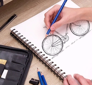 Close-up of hand sketching a bicycle on paper using a blue professional drawing pencil