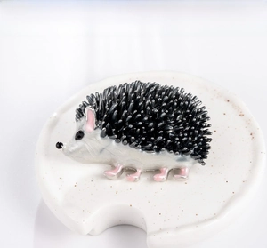 Macro shot of an enamel hedgehog brooch with black quills on a ceramic display base