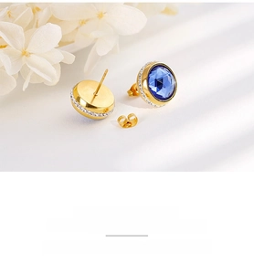 Detailed close-up of golden stud earrings with sapphire blue stone and zircon halo