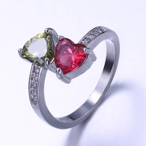 Macro detail of bypass ring featuring olive green and ruby red heart-shaped crystals