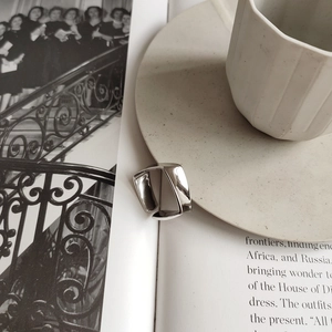 Close-up of a minimalist geometric silver ring on an open book with coffee
