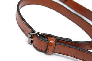 Gros plan d'une bandoulière en cuir marron avec boucle en métal foncé et surpiqûres