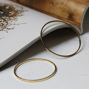 Detail view of two minimalist slim bangles in 18K gold plated finish on stone background