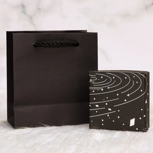 Black starry gift box and matching paper bag on a premium white marble background