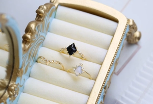 Dettaglio di anelli d'oro con opale nero e gemme in una scatola blu vintage