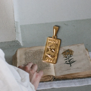 Rechteckiger Venus Münzanhänger mit 18K Goldbeschichtung auf antikem botanischem Buch