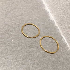 Minimalist gold-plated stainless steel hoop earrings on a grey textured stone surface
