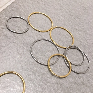 Minimalist gold and silver titanium steel hoop earrings in various sizes on marble surface