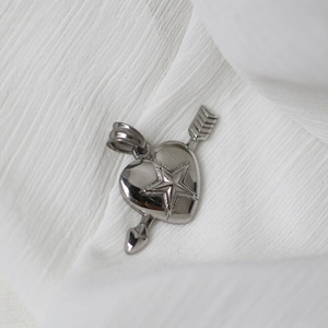 Detailed view of a silver heart pendant with arrow and star patterns on white fabric
