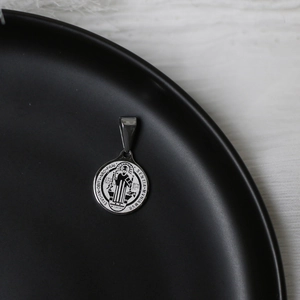 Macro shot of a vintage silver Saint Benedict medal pendant on a matte black display disk