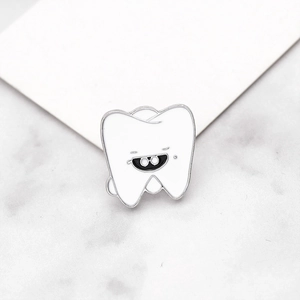 Macro shot of a cartoon tooth enamel pin with glasses on a marble surface