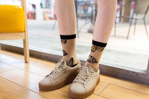 Close-up of beige crew socks with butterfly pattern and black cuffs on wood floor