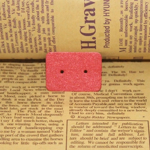 Detail of a pink glitter rectangular two-hole button placed on vintage newspaper background