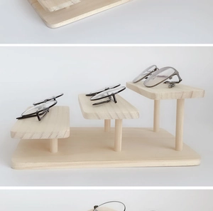 Three-tier wooden staircase stand displaying eyewear on a minimalist beige background