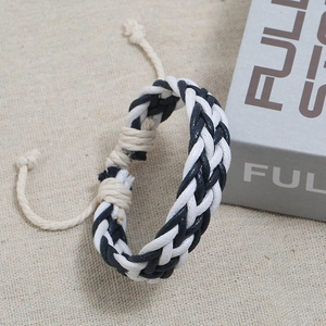 Detail of hand-woven black and white adjustable cotton cord bracelet on fabric
