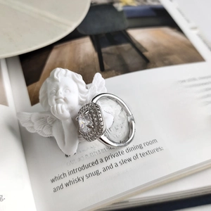Detail view of 925 silver halo ring with large square zircon on an angel statue background