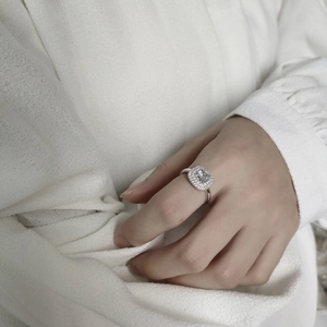 Detailed view of a silver square zircon ring worn by a model on white fabric