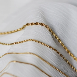 Close-up of assorted gold-plated titanium steel necklaces on white silk fabric