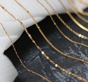 Macro shot of assorted gold titanium steel necklace chains on a textured stone and fabric background
