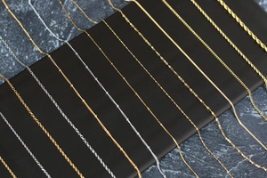 Detailed display of assorted gold and silver stainless steel chain styles on a black stand