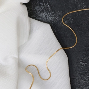 Detail of a 18k gold plated snake chain necklace on silk and stone background