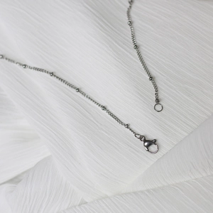 Close-up of silver steel necklace with bead details and lobster clasp on white fabric