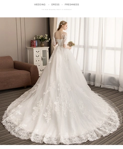 Detail of elegant white lace wedding dress featuring a long train and sheer half sleeves