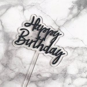 Detail of black Happy Birthday cursive font on transparent acrylic cake topper over marble