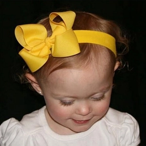 Infant girl wearing a bright yellow elastic headband with a large handmade bow decoration