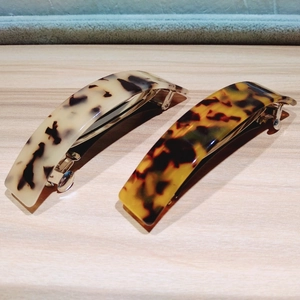 Detailed view of two leopard print hair clips in beige and amber resin on wood