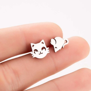 Detailed close-up of asymmetrical cat and mouse silver stud earrings held in fingers