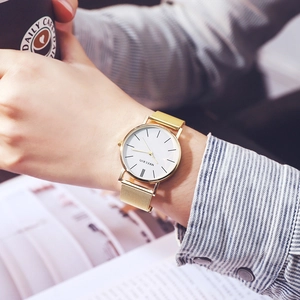 Minimalist gold mesh band watch with white dial shown in a business lifestyle setting